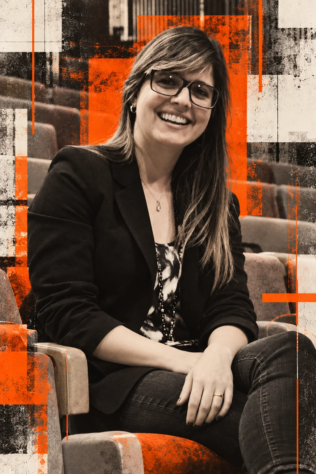Luciana Zaramela sorrindo, sentada em um auditório, de óculos e blazer, em retrato editorial preto e branco com laranja